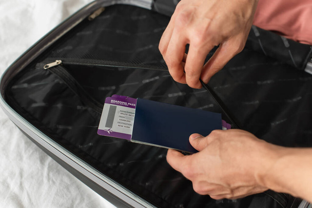 Cropped view of traveler putting boarding pass and passport in suitcase on bed  - Fotografie, Obrázek