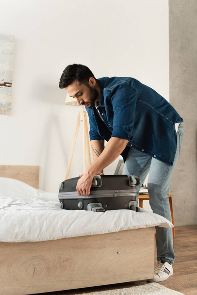 Bearded traveler fastening suitcase on bed at home  - Фото, изображение