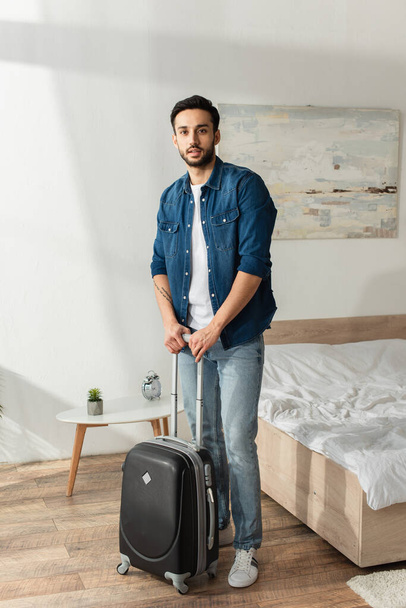 Nuori mies matkalaukku katselee kameraa makuuhuoneessa  - Valokuva, kuva