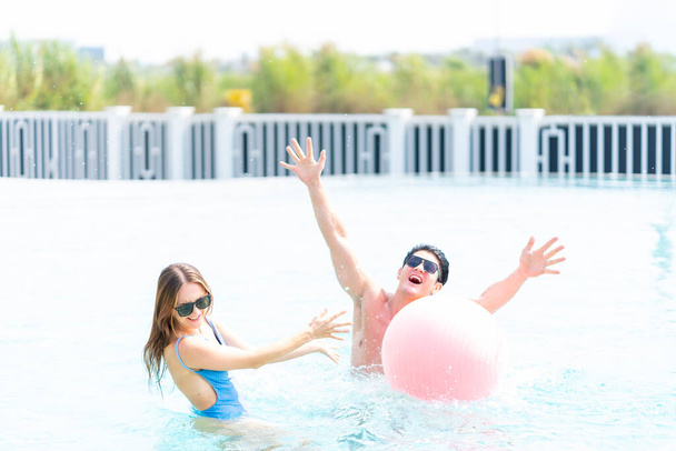 Muž a žena si hrají v bazénu s plážovým míčem. Mladý pár objímající se v bazénu. - Fotografie, Obrázek