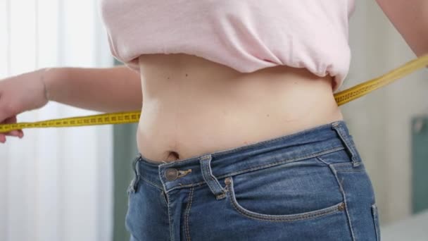 Νεαρή γυναίκα με τζιν που μετράει τη λεπτή επίπεδη μέση της με μεζούρα. Έννοια της δίαιτας, απώλεια βάρους και υγιεινό τρόπο ζωής. - Πλάνα, βίντεο