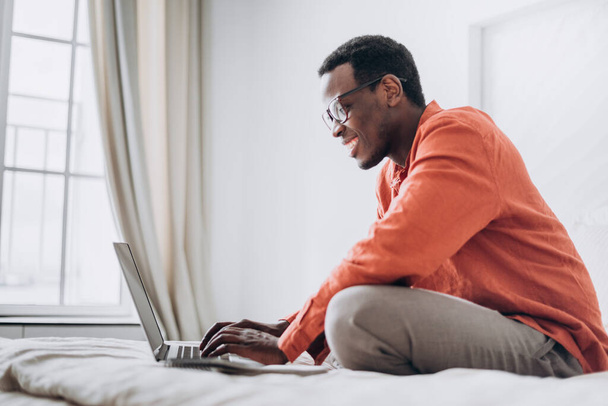 Afro-Amerikaanse man freelancer werkt op laptop op bed - Foto, afbeelding