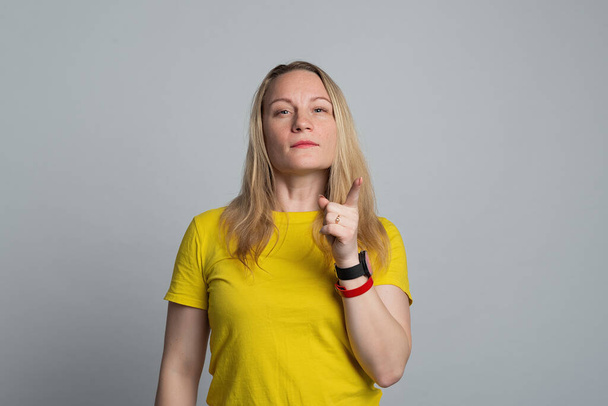 Портрет женщины в повседневной желтой футболке, показывающий жест внимания. Концепция жеста. Студийный снимок, серый фон - Фото, изображение