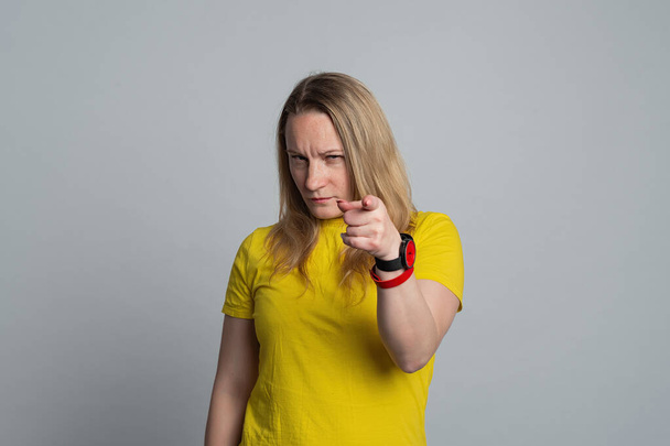 Žena ukazující nespokojeně a frustrovaně na kameru, naštvaná a rozzuřená na tebe, oblečená v nenucené žluté tričko. Skutečné lidské reakce, emoce a pocity. Studio záběr, šedé pozadí - Fotografie, Obrázek