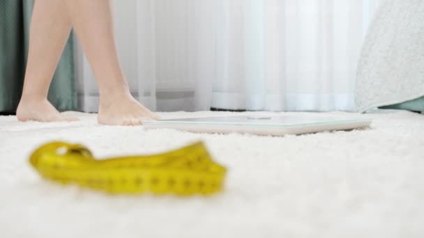 Camera focusing on measuring tape and woman weighting on scales at bedroom. Concept of dieting, loosing weight and healthy lifestyle. - Footage, Video
