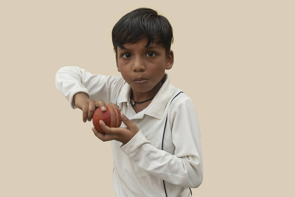 Ένα αγόρι με στολή κρίκετ, πασπαλισμένο μπόουλινγκ. - Φωτογραφία, εικόνα