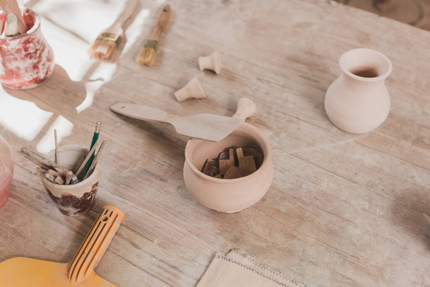 木製のテーブルの上にへらや陶器の機器と手作りの粘土鍋の高い角度ビュー - 写真・画像