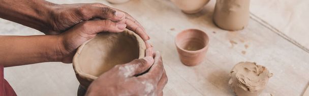 vue partielle du jeune couple afro-américain sculptant pot d'argile avec les mains jointes dans la poterie, bannière - Photo, image