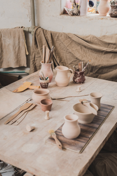 陶器の木製テーブルの上の機器の近くに手作りの粘土鍋の高い角度ビュー - 写真・画像