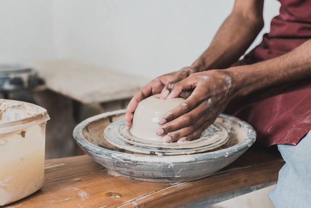 partial view of young african american man modeling wet clay on wheel with hands in pottery - Fotoğraf, Görsel
