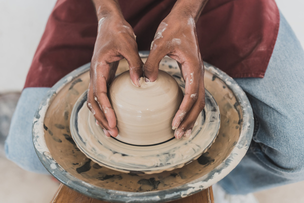 close up view of young african american man modeling wet clay on wheel with hands in pottery - Photo, Image