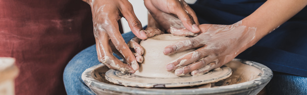 partial view of young african american couple modeling wet clay on wheel with hands in pottery, banner - Fotoğraf, Görsel