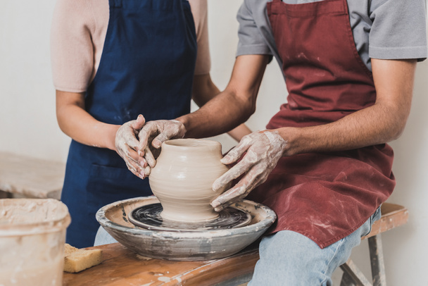 partial view of young african american couple modeling wet clay pot on wheel with hands in pottery - Photo, Image