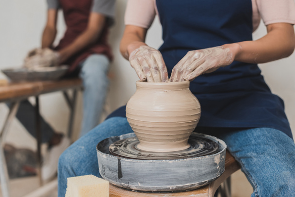 vista parziale della giovane coppia afroamericana in grembiuli che lavora con vaso di argilla su ruota in ceramica - Foto, immagini