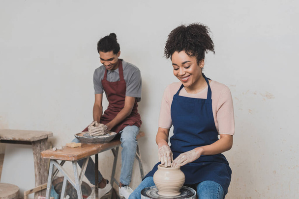 mosolygó fiatal afro-amerikai pár kötényben dolgozik nedves agyag edények fazekas - Fotó, kép