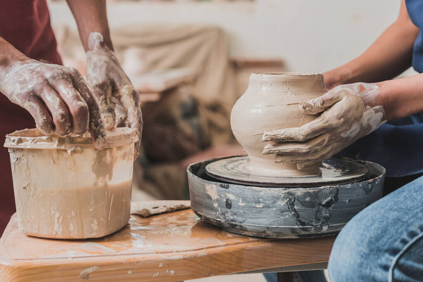 partial view of young african american couple sculpting pot on wheel near plastic box with water in pottery - Photo, Image