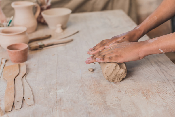 częściowy widok żeńskich afrykańskich rąk wytaczających kawałek gliny na drewnianym stole w ceramice - Zdjęcie, obraz