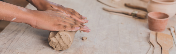 vista parcial de las manos afroamericanas hembras desplegando pieza de arcilla en la mesa de madera en cerámica, pancarta - Foto, Imagen