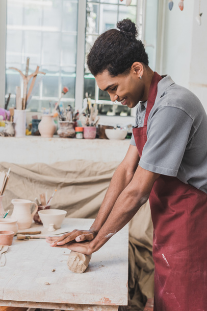 sorridente giovane afroamericano in grembiule che lavora con argilla in ceramica - Foto, immagini