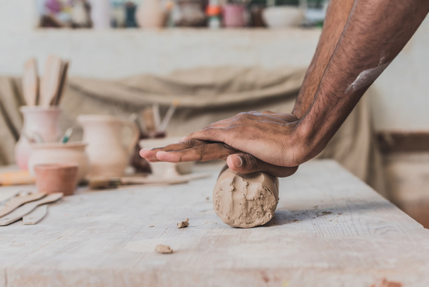 manos afroamericanas masculinas trabajando con arcilla sobre mesa de madera en cerámica - Foto, Imagen