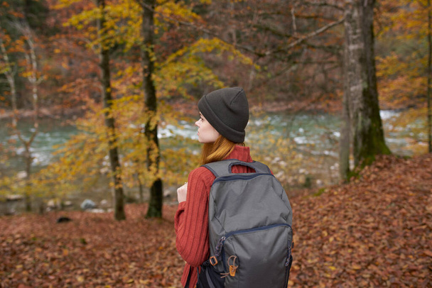 traveler with a backpack and in a gray hat in the autumn forest fallen leaves trees river model - Foto, immagini