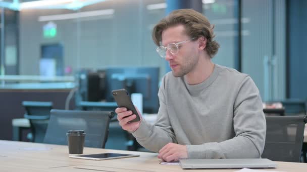 Fiatal üzletember reagál a veszteségre okostelefonon az irodában  - Felvétel, videó