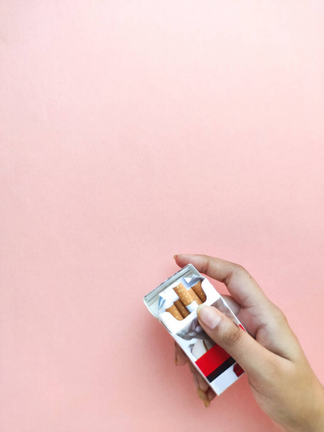 A vertical shot of a person holding a pack of cigarettes against a pink background - Photo, image