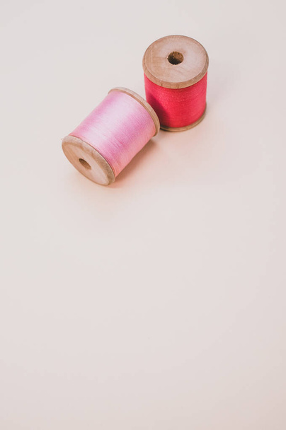 A closeup of pink and red sewing threads isolated on a light background with free space for text - 写真・画像
