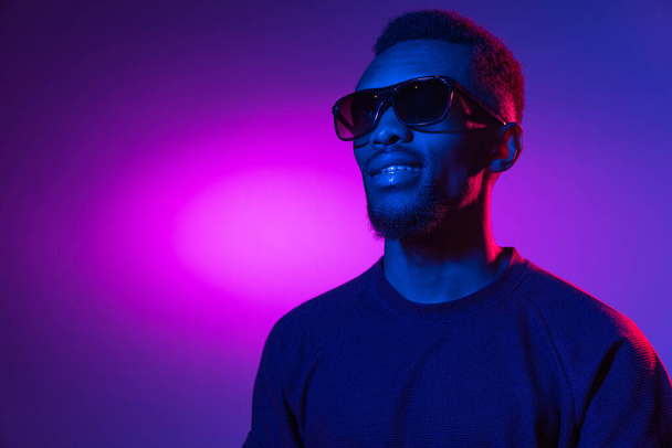 African-american young mans portrait on dark studio background in neon. Concept of human emotions, facial expression, youth, sales, ad. - Photo, Image