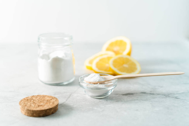 Eco friendly natural cleaners, jar with baking soda, lemon and wooden spoon on marble table background. Organic ingredients for homemade cleaning. Zero waste concept - Photo, Image