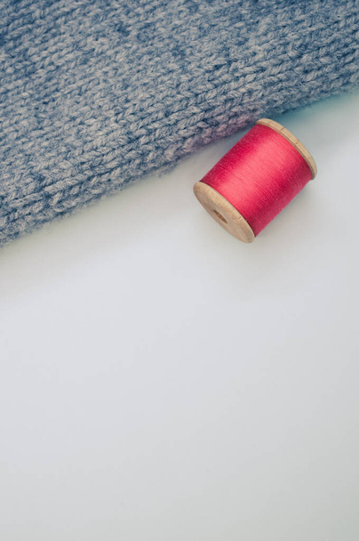 白い背景にグレーの布の横にある赤い縫製糸で、テキスト用の空きスペースがあります。 - 写真・画像