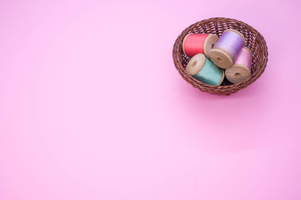 A basket of colorful sewing threads isolated on a pink background with free space for text - Photo, image