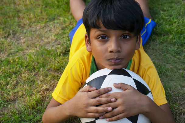 Mladý chlapec ležící v zemi s fotbalem - Fotografie, Obrázek