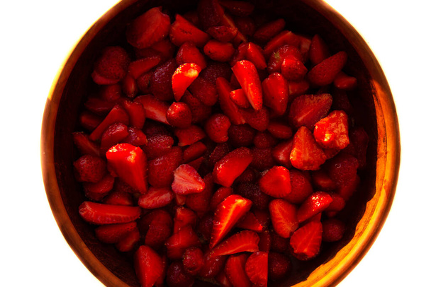 Κόκκινη υφή φόντου από φράουλες σε φέτες. Ώριμη φέτα φράουλας σε ξύλινο μπωλ σε λευκό φόντο. φέτες φράουλας. Φρέσκα μούρα. Φόντο φρούτων. Άνω όψη - Φωτογραφία, εικόνα