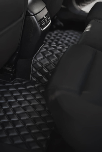 Autovloermat met diamantpatroon. Ecoleather dark floormat op de tweede rij in het moderne voertuig. transmissietunnel op de passagiersstoel in het voertuig. concept van luxe en schone auto - Foto, afbeelding