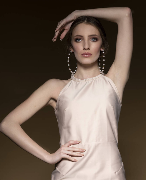 elegant dressed girl in beige outfit , she is posing on dark background , she has very big pearl earrings - Zdjęcie, obraz