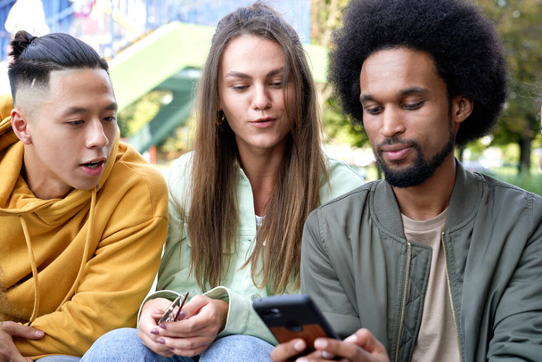 Close up of three young people with mobile phone outdoors - Photo, Image