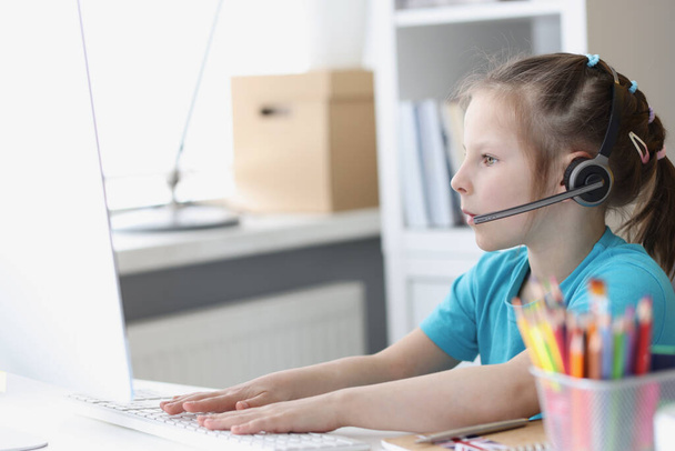 Little girl at computer in headphones with microphone works at computer. - Photo, Image