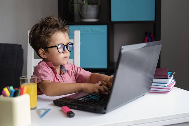 κουρασμένος καυκάσιος αγόρι χρησιμοποιώντας φορητό υπολογιστή με γυαλιά που σπουδάζουν στο σπίτι - Φωτογραφία, εικόνα