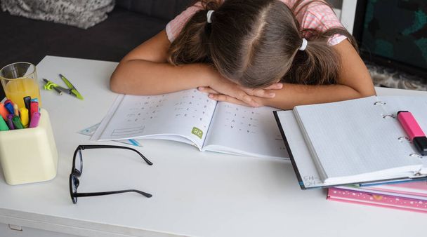 Müdes, erschöpftes Mädchen liegt auf ihren Händen und macht Hausaufgaben - Foto, Bild