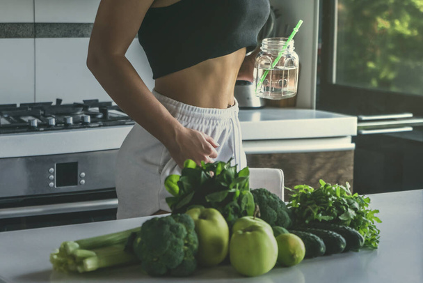 Fit woman drinking water, preparing vegetables for Green detox smoothie. Raw food diet. - Фото, зображення