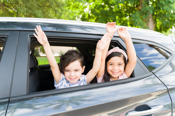 Adorable brother and sister raising their arms and feeling excited while playing inside the car before a family road trip with their parents - Fotoğraf, Görsel