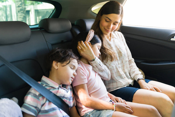 Entzückende Kinder, die mit ihrer Mutter auf der Heimfahrt nach einem Ausflug im Auto schlafen. Müde junge Geschwister kuscheln mit ihrer Mutter  - Foto, Bild