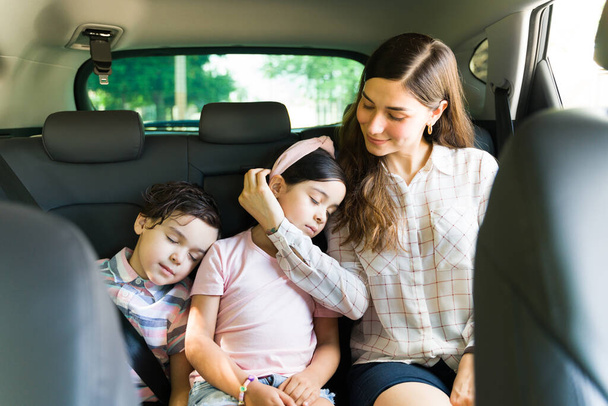 Bütün gün dışarıda oynadıktan sonra anneleriyle arabada uyuyakalan yorgun çocuklar. Değer veren genç bir kadın ve anne kızının yüzünü okşuyor. - Fotoğraf, Görsel