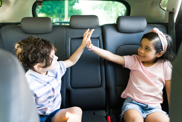 ¡Choca esos cinco! Hermoso niño y niña latina elemental divirtiéndose y haciendo una alta cinco mientras se sienta dentro del coche  - Foto, imagen