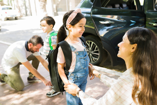 Izgatott vagyok az iskola miatt. Csinos fiatal lány mosolyog a gyönyörű anyukájára, miután kiszállt a kocsiból, hogy iskolába járjon a kisöccsével. - Fotó, kép