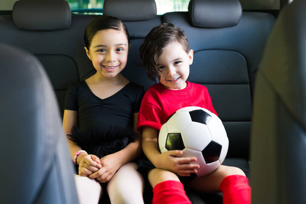 Uwielbiam lekcje pozalekcyjne. Uroczy brat i siostra siedzą w samochodzie podczas jazdy na lekcje tańca baletowego i piłki nożnej  - Zdjęcie, obraz