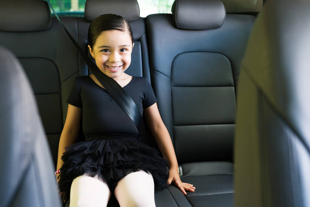 Me encanta el ballet. Hermosa niña con una falda negra sentada en el coche y sonriendo en su viaje a sus clases de baile de ballet - Foto, imagen