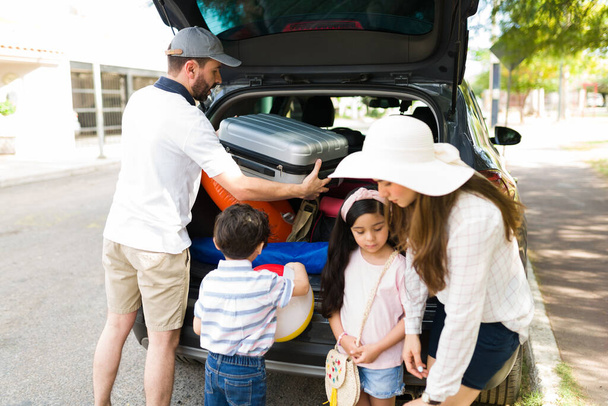 Menino e menina bonito ajudando seus pais a arrumar suas malas e coisas no carro antes de ir em uma viagem de carro em família durante as férias de verão - Foto, Imagem