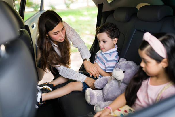 Να είσαι καλός και να είσαι ασφαλής. Αγαπώντας τη νεαρή μαμά που δένει τη ζώνη ασφαλείας των παιδιών της στο αυτοκίνητο πριν πάει σε ένα οικογενειακό οδικό ταξίδι - Φωτογραφία, εικόνα